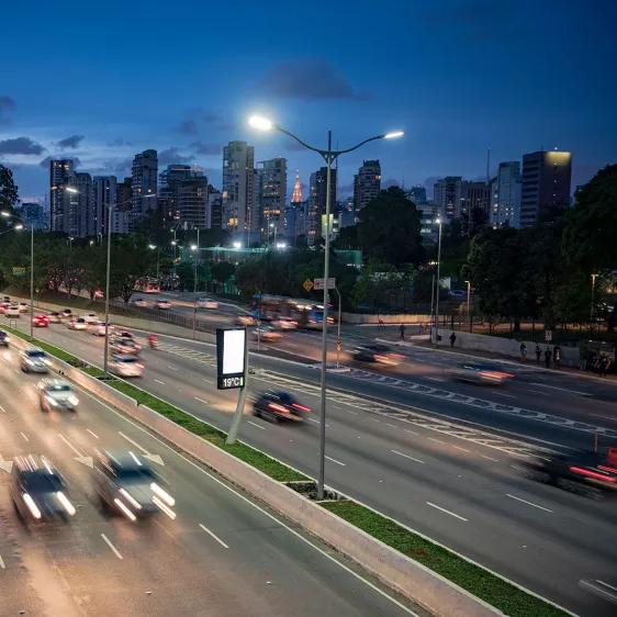 Postes de luz iluminando uma avenida movimentada de carros