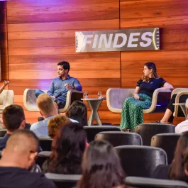 Sala cheia de ouvintes, com 4 pessoas em cima de um palco discursando sobre inovação